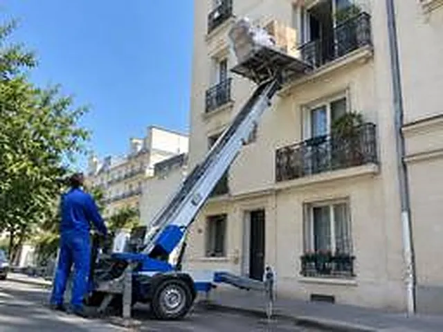 Monte-meubles hissant un fauteuil jusqu'au balcon d'un immeuble